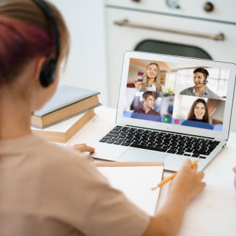 A girl is communicating via video call with classmates on laptop at home
