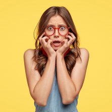 concerned-nervous-timid-woman-keeps-hands-cheeks-looks-with-frightened-expression-wears-optical-glasses-feels-worried-as-made-mistake-has-insecure-expression-isolated-yellow-wall (1)